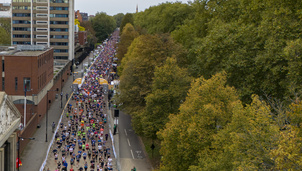 Aerial view of a large group of participants crossing the start of the Royal Parks Half Marathon, along a city street surrounded by autumn trees and urban buildings.